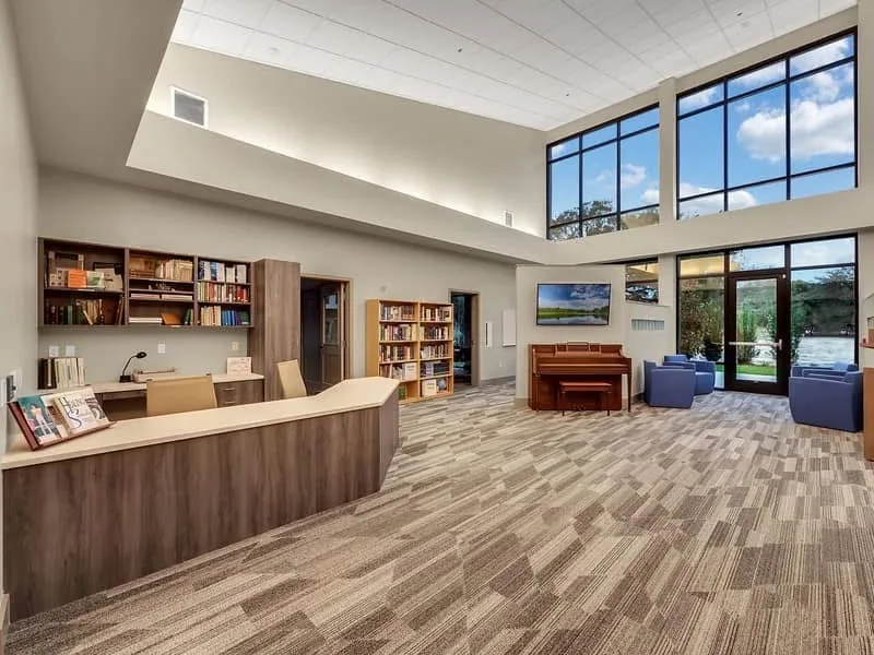 Double-height reading room with tall windows, bookshelves and a stepped ceiling plane.